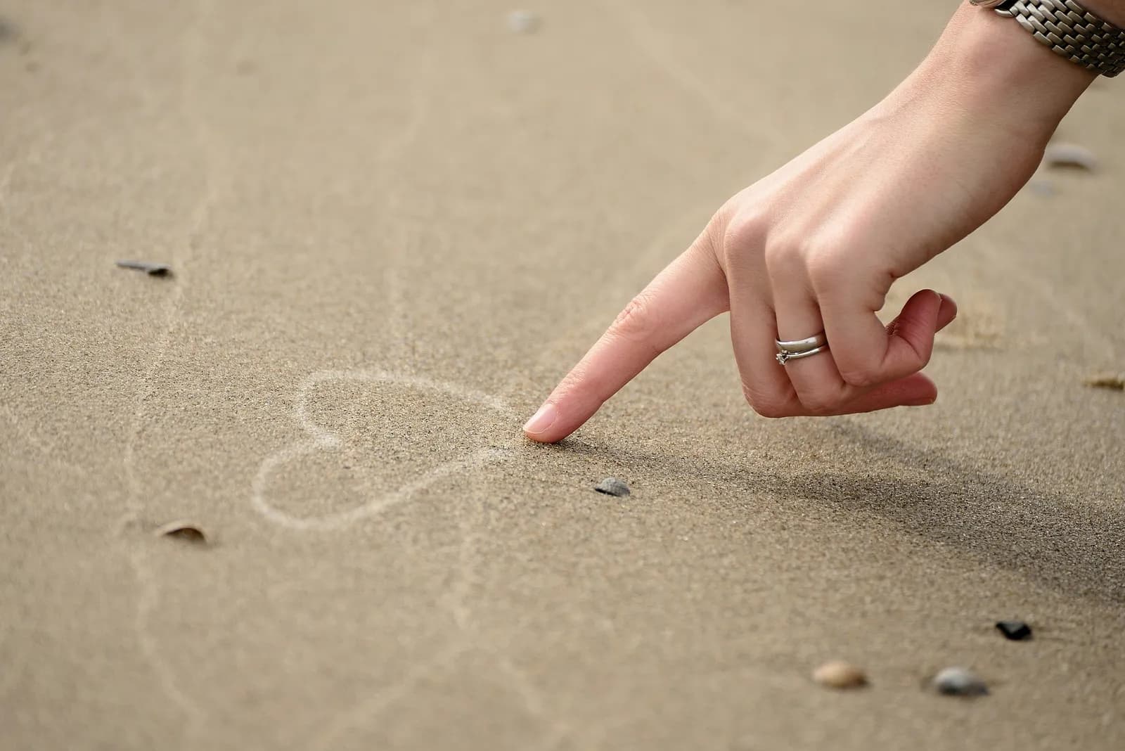 Een hand tekent een hart in het natte zand op het strand