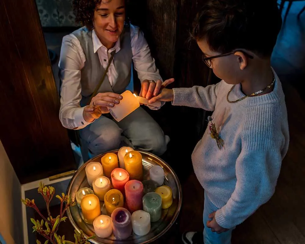 Annemarie Voogt geeft een brandende kaars aan een jongen, bij een schaal met kaarsen