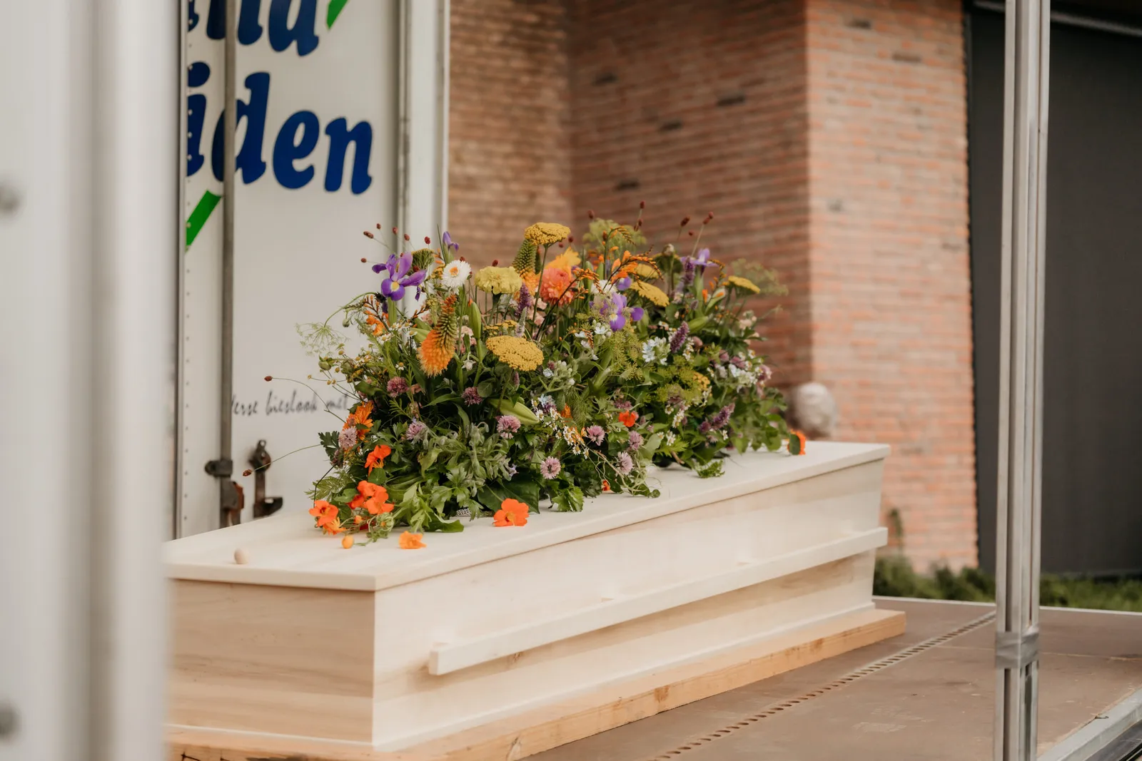 De kist met een kleurrijk bloemstuk, klaar voor de laatste rit
