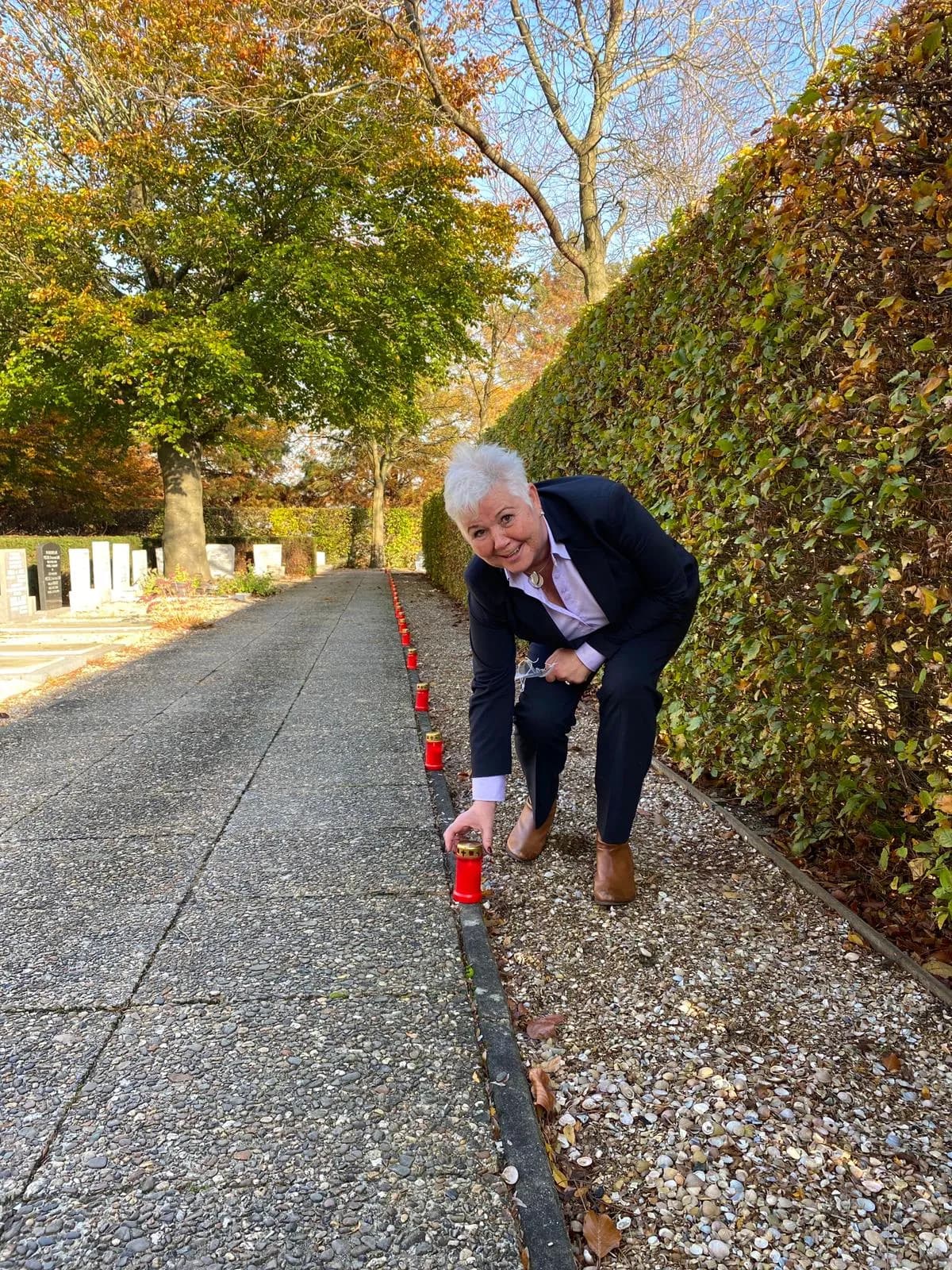 Els zet gebukt een brandende kaars neer langs het pad