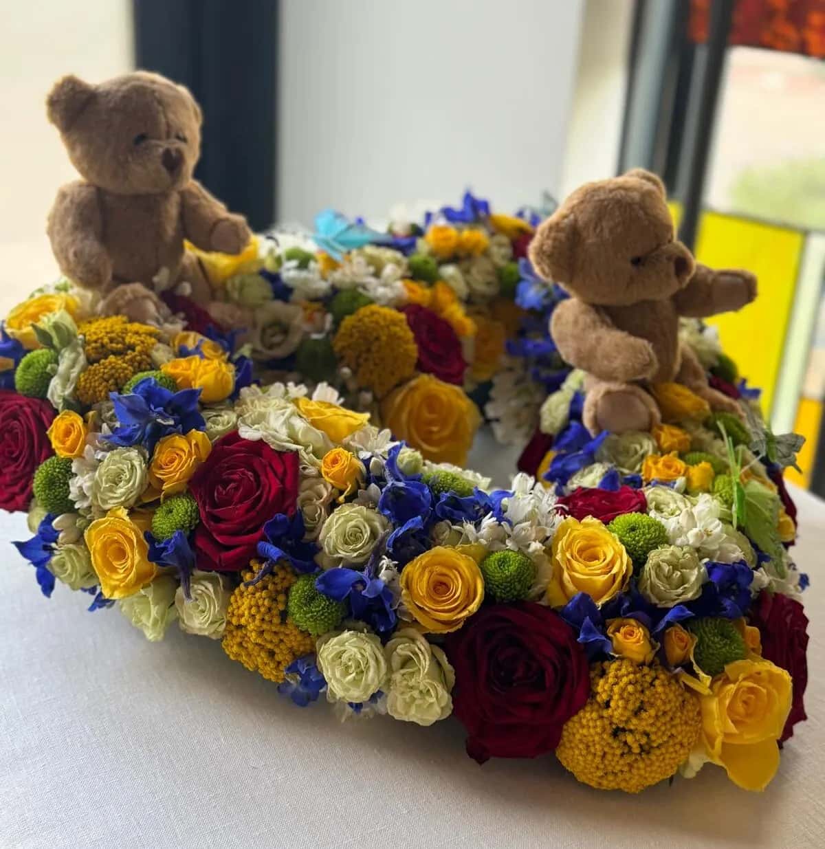 Kleurrijk bloemstuk met twee teddyberen op de kist