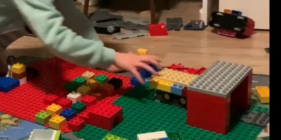 Kind speelt de uitvaart na met duplo: een kist op een wagentje rijdt een rood gebouwtje in