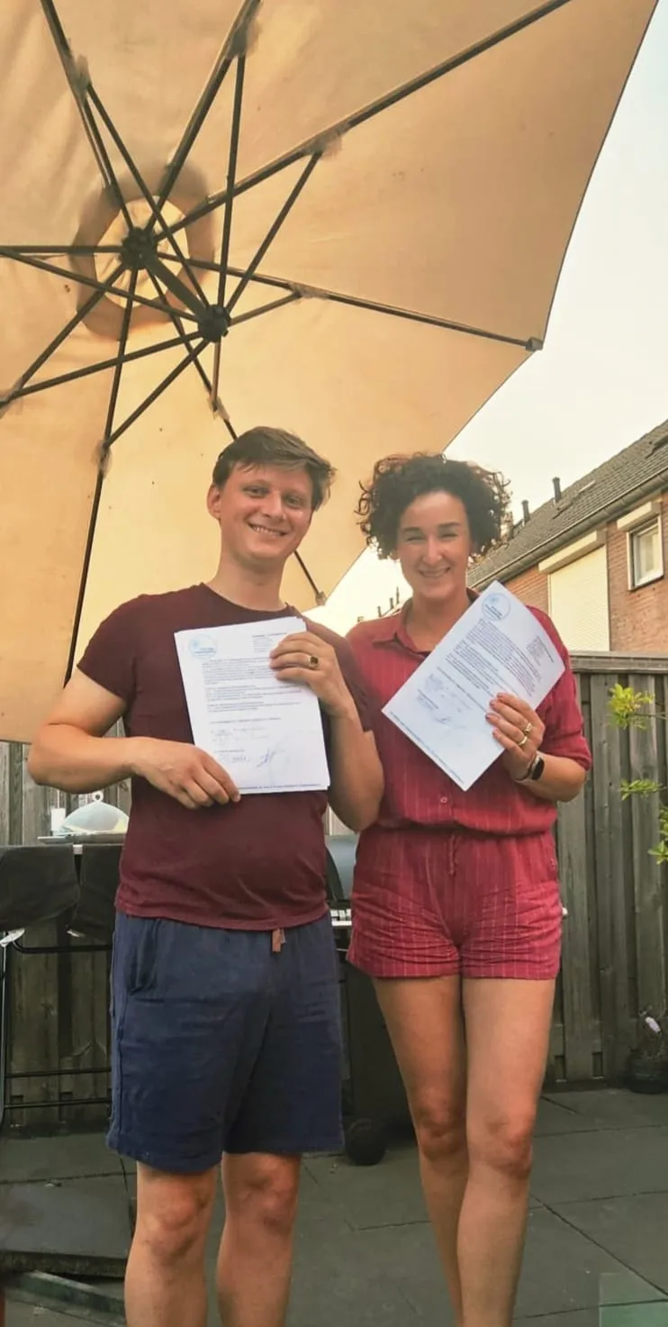 Frank en Annemarie in de tuin onder een parasol, elk met een ondertekend contract in de hand